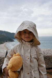 Portrait of girl wearing jacket standing against sea