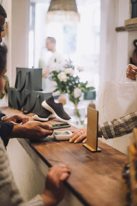 Cropped hands of customer and retail clerk with smart phone at checkout in boutique