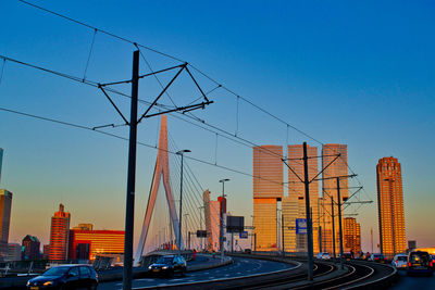 Cars on road by buildings against clear sky during sunset