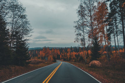 Empty road along trees in forest against sky