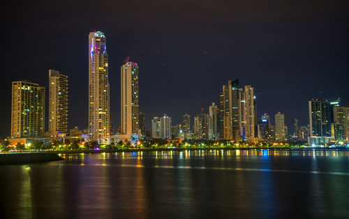 Illuminated modern buildings in city against sky at night, long exposure