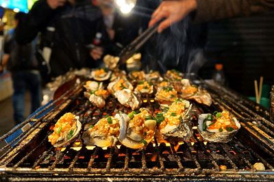 Cropped hand preparing seafood on barbecue grill at market