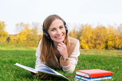 Portrait of smiling young woman listening music while lying on grassy field