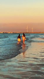 People on beach against sky during sunset