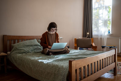 Young woman sitting on bed at home