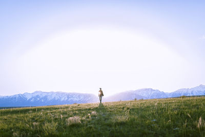 Female hiker standing on grassy field against mountains