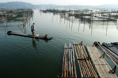 Rear view of man standing on wooden raft in sea