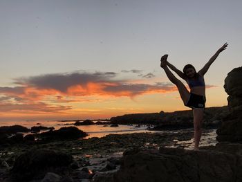 Woman standing on rock against sky during sunset