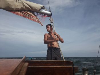 Man standing on sailboat by sea against sky