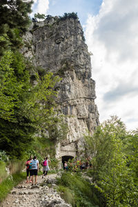 People hiking on rock formation against cloudy sky