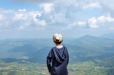 Rear view of boy standing against mountains and sky