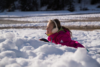 Smiling girl lying on snow covered land