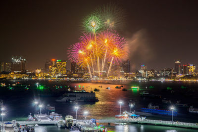 Firework display over illuminated city against sky at night