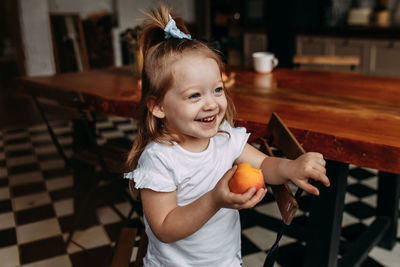 Funny little girl child in pajamas holding and eating an apple and laughing in the kitchen at home