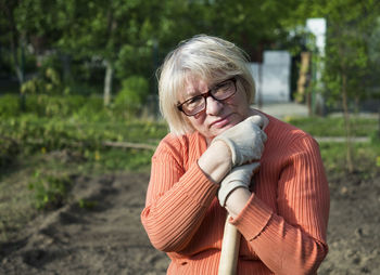 Portrait of mature woman with shovel standing at yard
