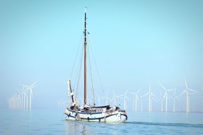 Sailboat with wind turbines in sea against clear sky
