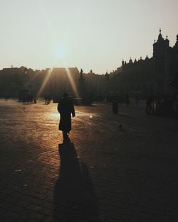 Silhouette people walking in town square during sunset