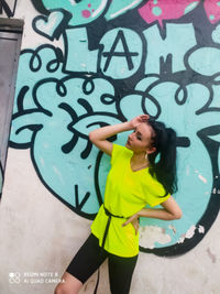 Full length of happy boy standing against graffiti wall