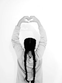 Rear view of woman making heart shape towards white background