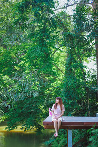 Woman sitting on bench against trees