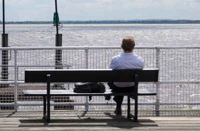 Rear view of man sitting on bench against sea