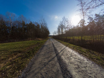 Empty road along trees and plants against sky