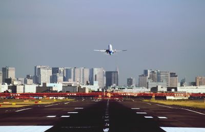 Airplane flying over road in city against sky