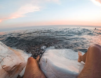 Low section of person in sea against sky during sunset