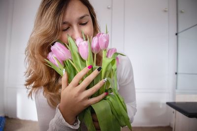 Close-up of woman smelling tulips while standing against wall at home