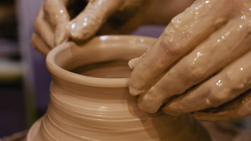 Cropped hands of craftsperson making clay product in pottery workshop