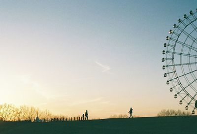 Silhouette people by ferris wheel against sky