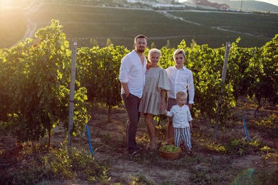 Family with children, boys, stands in a grape field at sunset with a basket of green berries