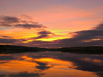 Scenic view of lake against dramatic sky during sunset