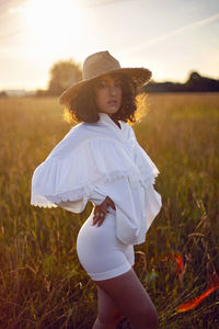  portrait of a curly-haired woman in white clothes and in a wicker hat stand on a field  in autumn