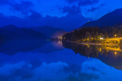 Scenic view of lake by mountains against blue sky at dusk