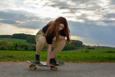 A young girl squats skateboarding on a road in green nature