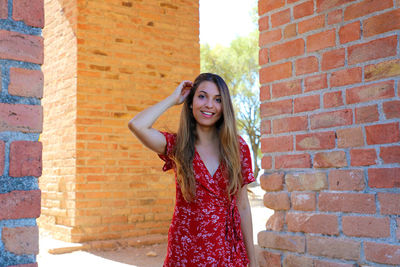 Portrait of beautiful young woman standing against brick wall