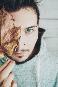 Close-up portrait of young man holding leaf on face