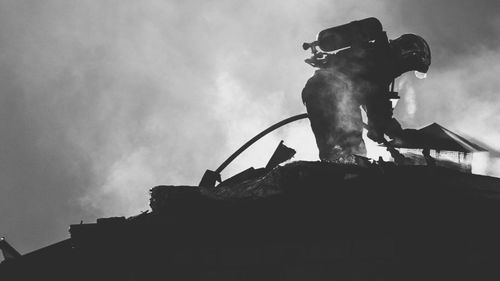 Low angle view of fireman spraying water on roof against sky