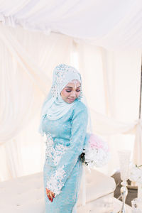 Smiling young woman in traditional clothing standing against seat