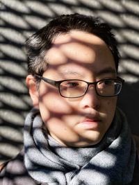 Close-up portrait of young man in eyeglasses against wall with strong sunlight and shadow patterns.