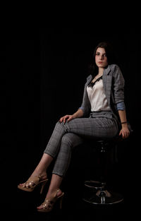 Portrait of young woman sitting on seat against black background