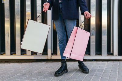 Crop unrecognizable female buyer standing in street with paper bags after shopping in city