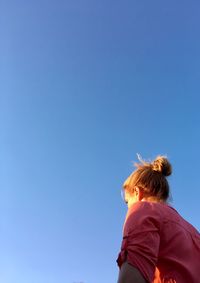 Low angle view of woman standing against clear blue sky