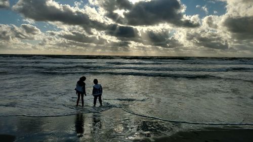 Silhouette friends standing on beach against sky during sunset