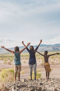 Full length rear view of people with arms raised against sky