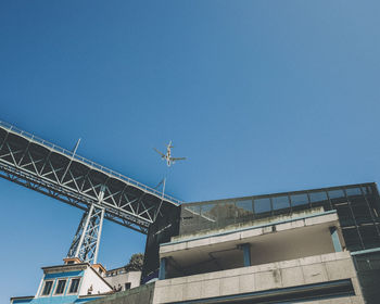 Low angle view of airplane flying by building against clear blue sky