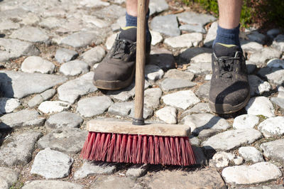 Gardener in dirty work clothes and boots holds garden tools, plastic brush broom