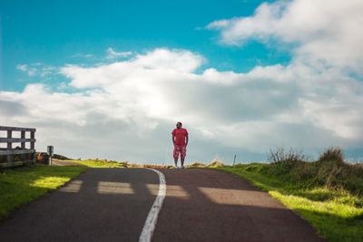 Rear view of man walking on road against sky