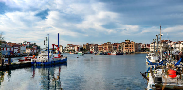 Sailboats moored in harbor by buildings in city against sky